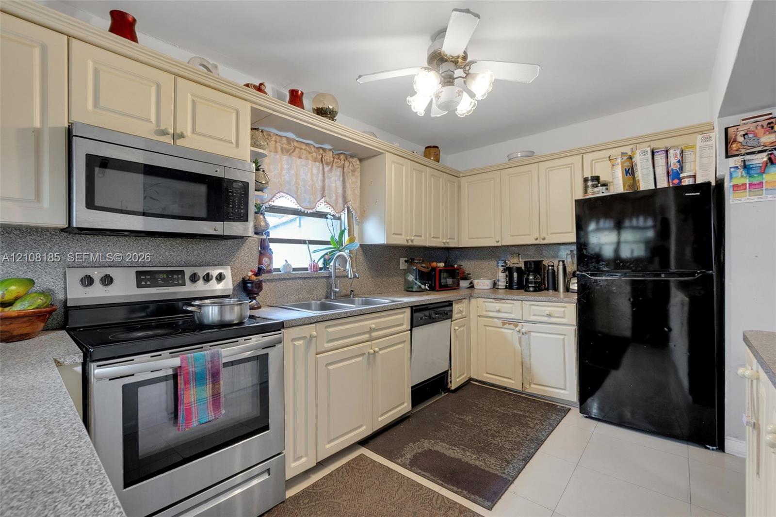 Kitchen featuring light-toned cabinetry, solid surface countertops, stainless steel appliances, and an integrated dual-basin sink with a gooseneck faucet