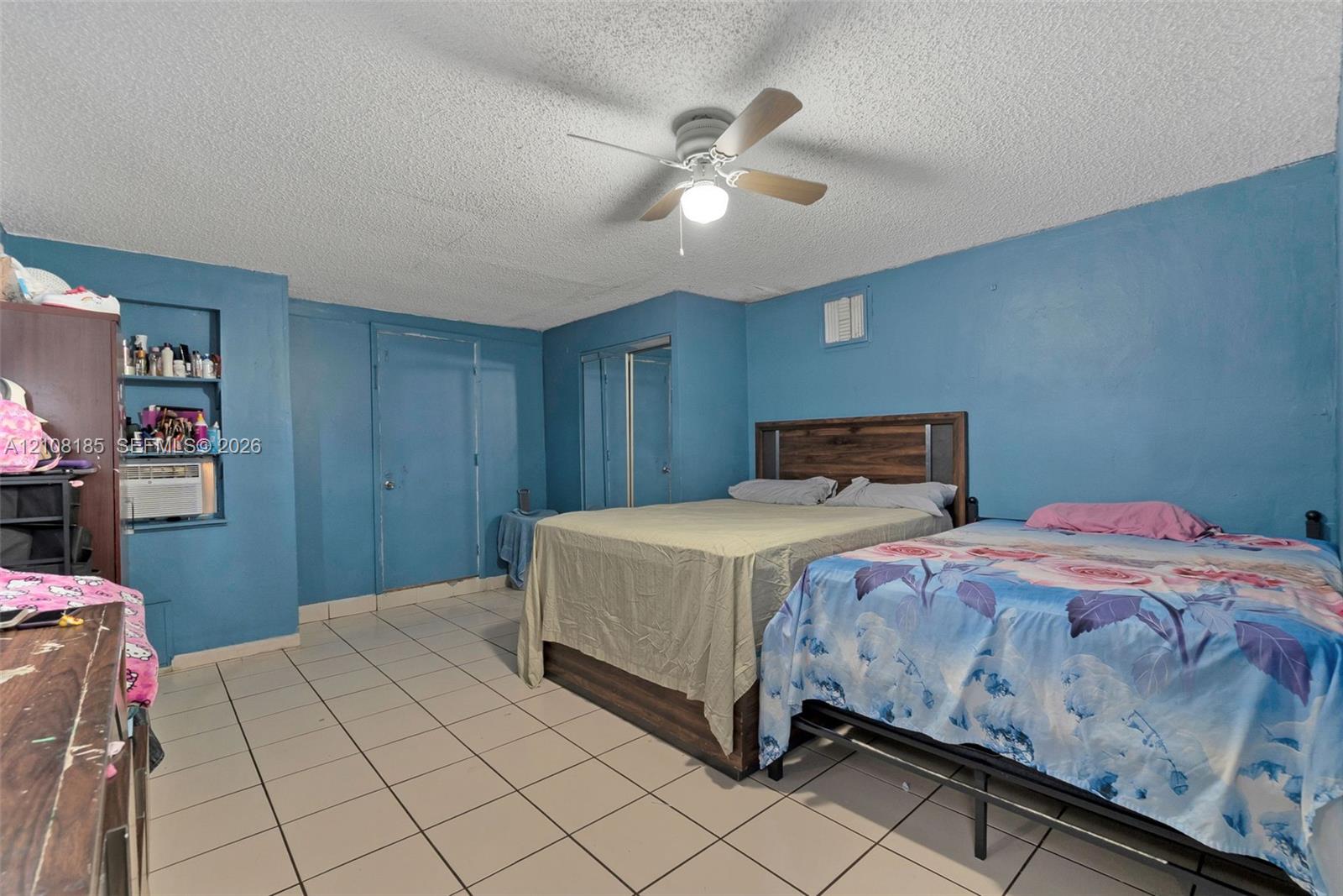 Room featuring white tile flooring, a ceiling fan with light fixture, built-in shelving, and mirrored closet doors