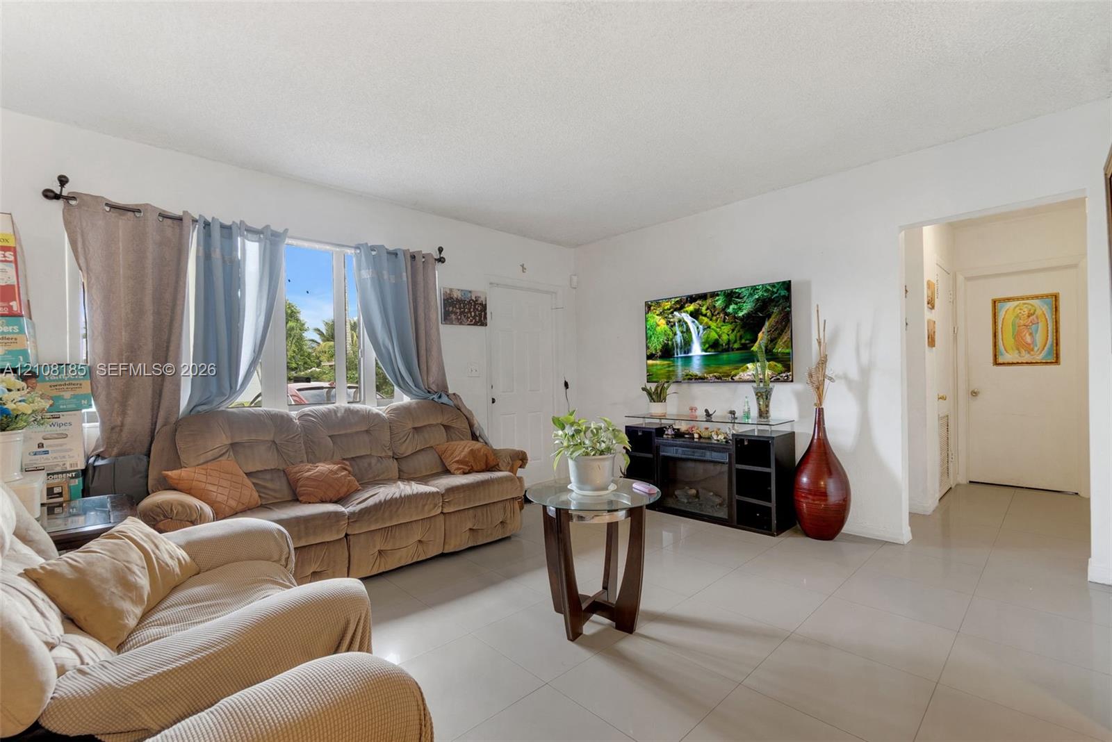 Living area featuring large windows with natural light, neutral wall-to-wall tile flooring, and a textured ceiling