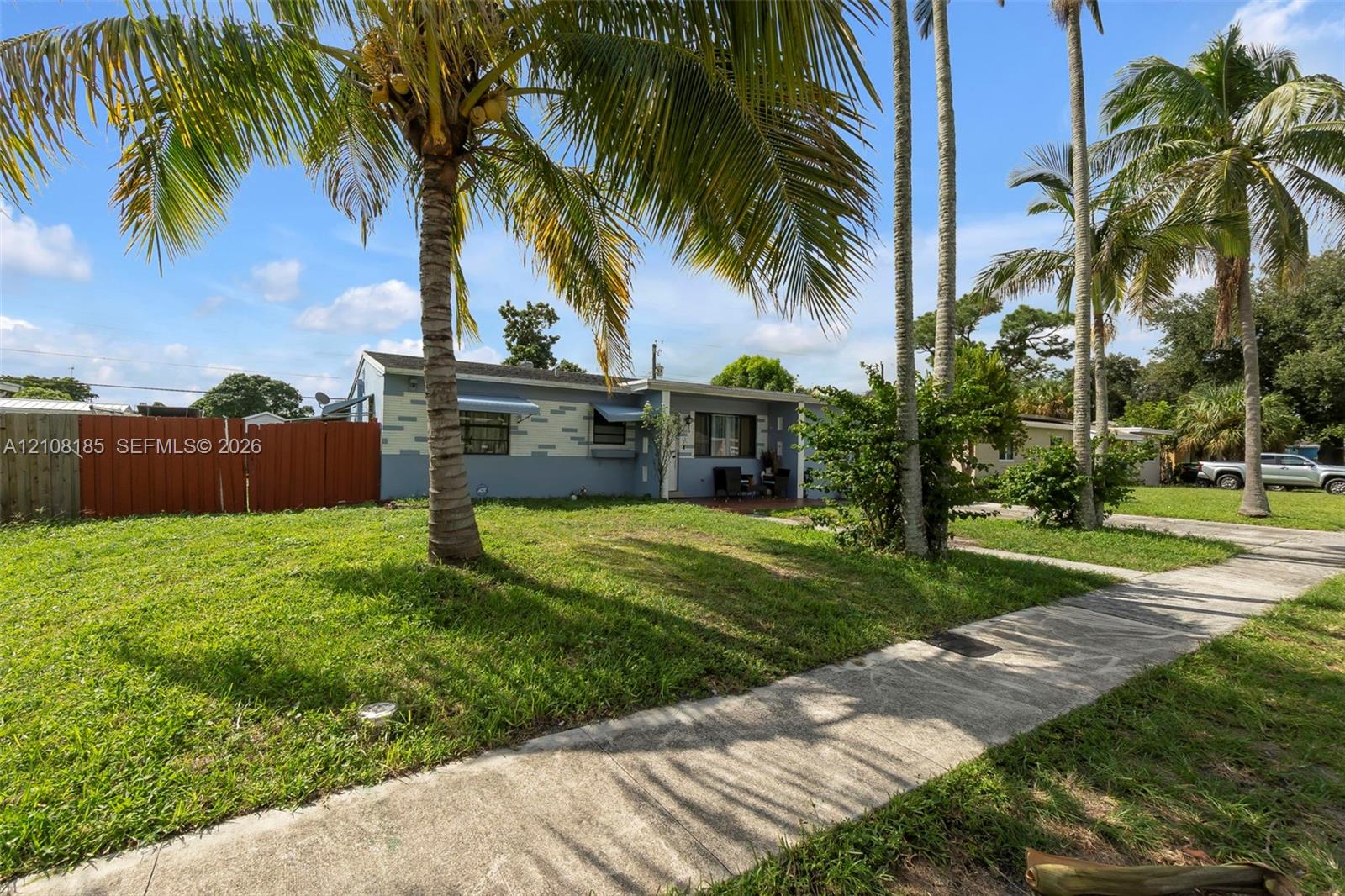 Exterior facade featuring painted masonry, horizontal siding, mature palm trees, a concrete walkway, and a privacy fence