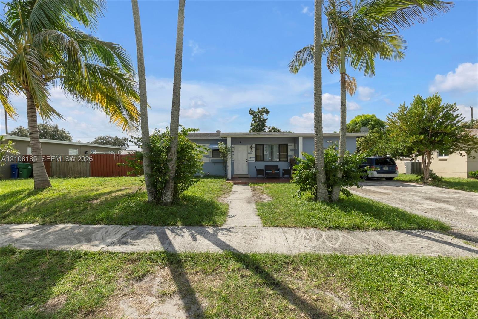 Single-story exterior featuring a flat roofline, covered front porch, concrete driveway, and established palm trees
