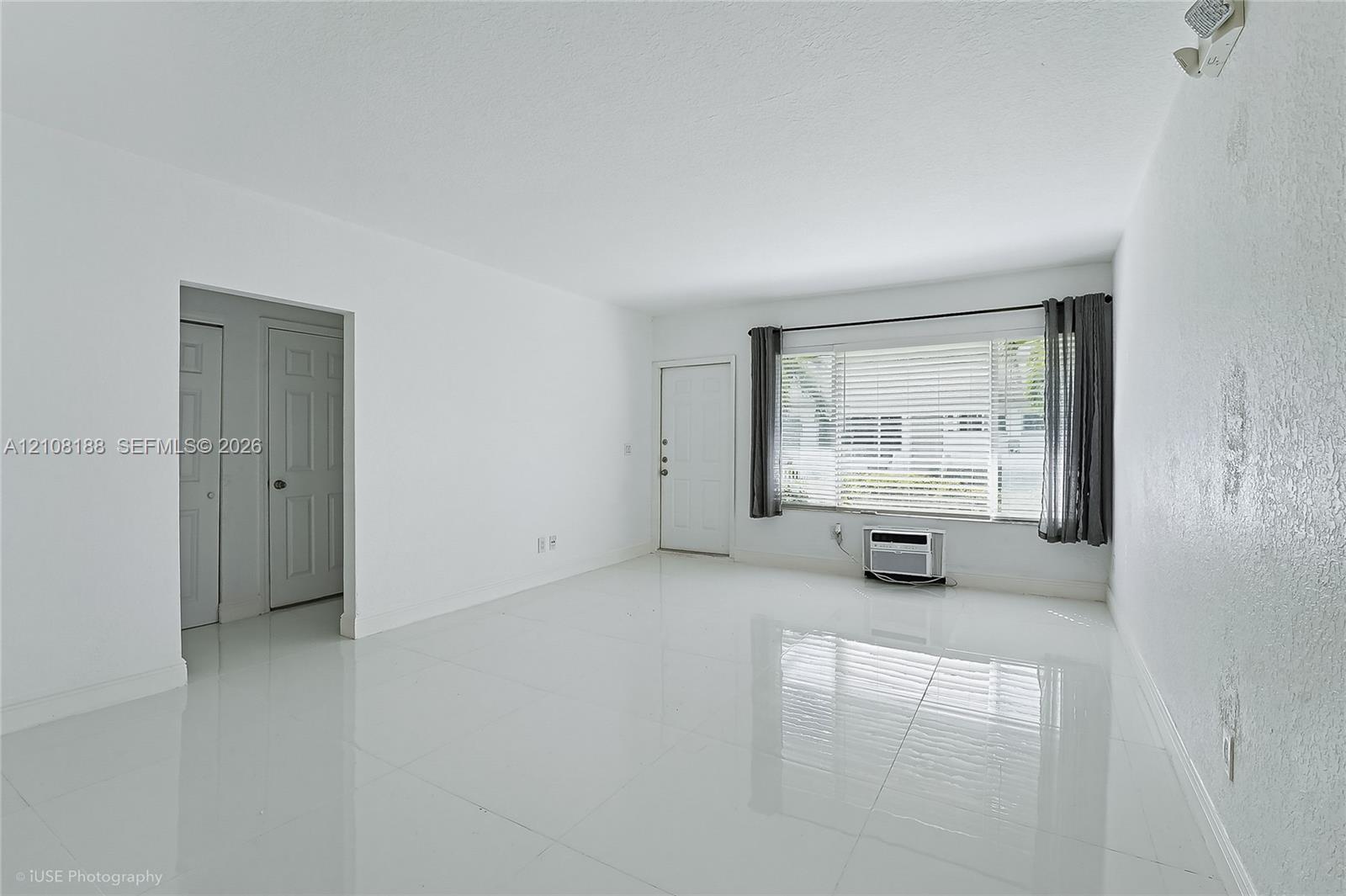 Bright interior space featuring polished tile flooring, a large picture window with horizontal blinds, and a wall-mounted air conditioning unit