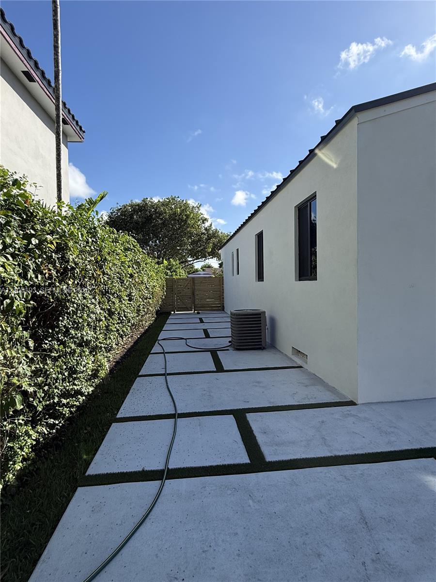 Exterior side yard featuring a concrete paver walkway with integrated turf lines, a mature hedgerow, and a wood-slat privacy screen