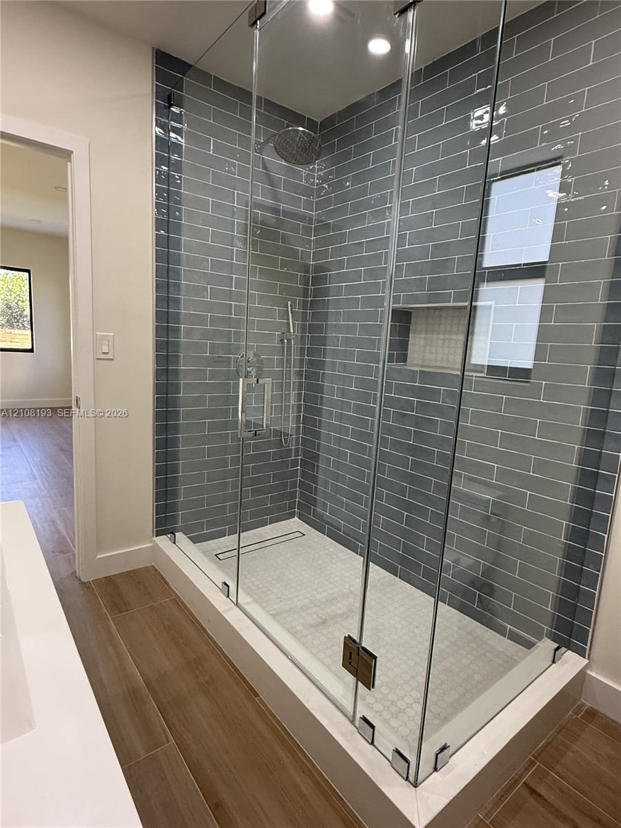 Walk-in shower featuring gray subway tile walls, a frameless glass enclosure, recessed wall niche, linear floor drain, and rainfall showerhead