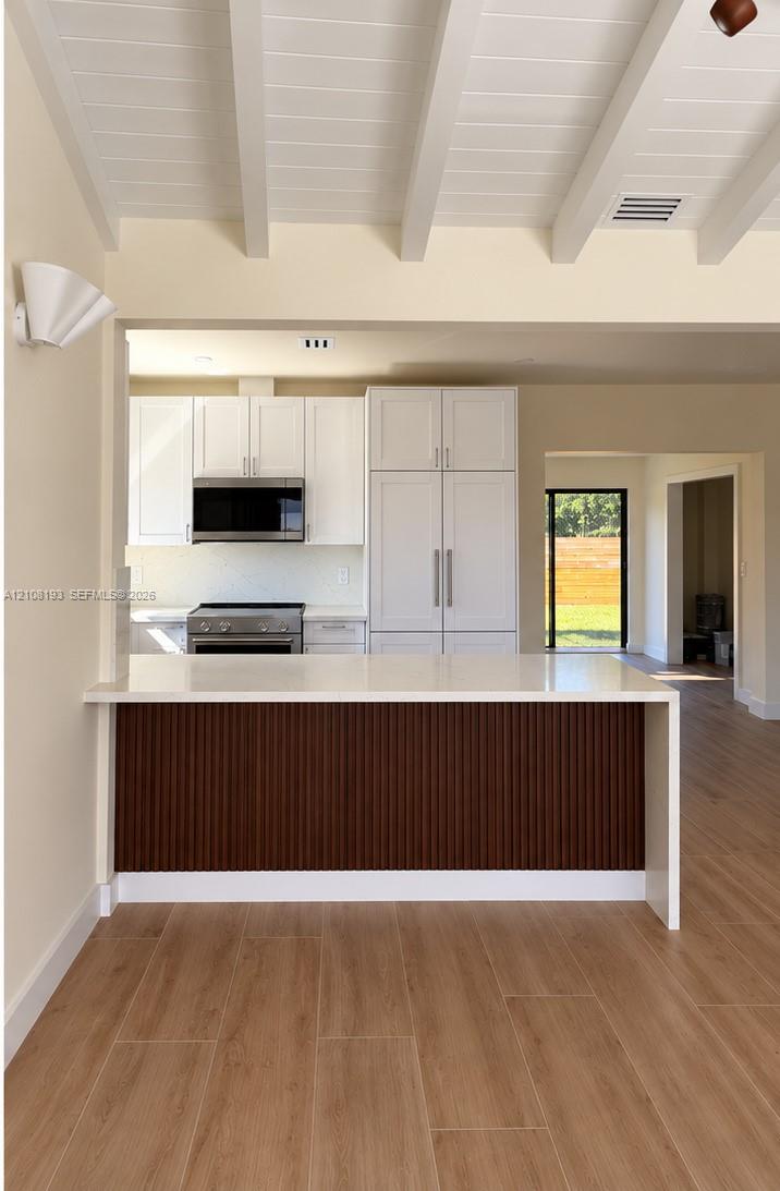 Kitchen featuring white cabinetry, wood-finish flooring, a quartz countertop, and a paneled breakfast bar with exposed ceiling beams