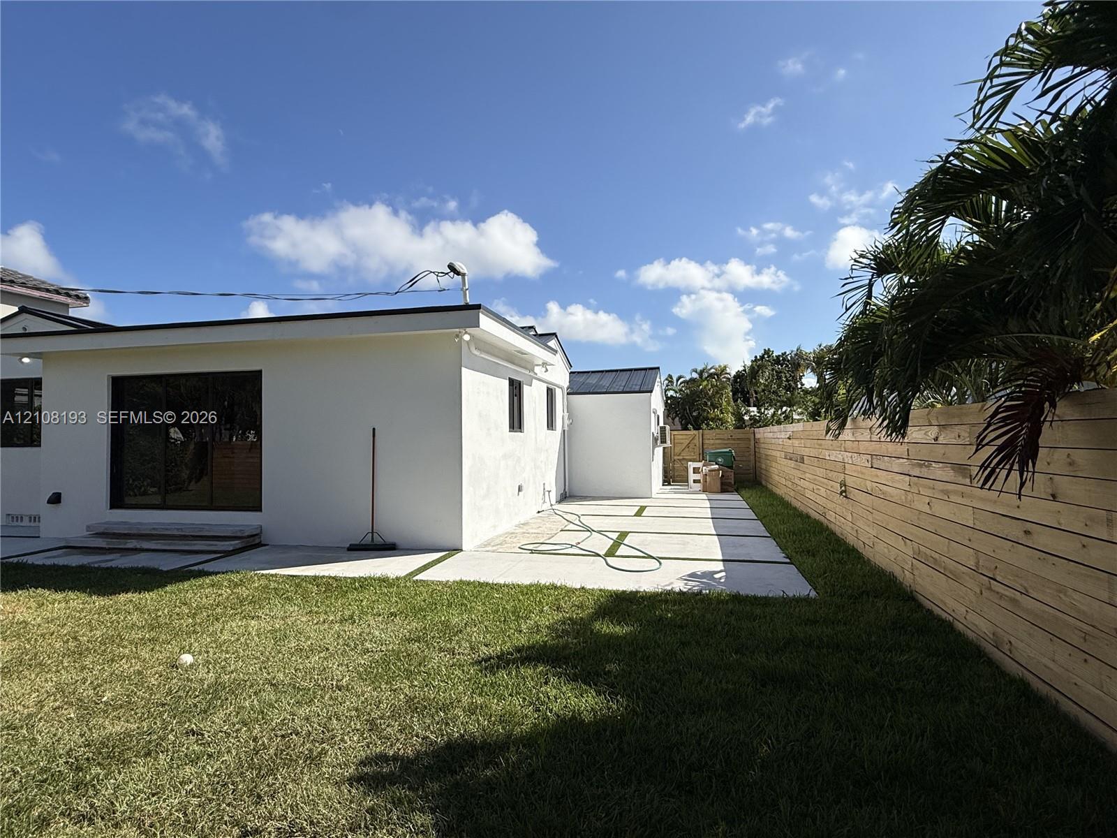 Backyard featuring a paved stone patio with grass inlays, horizontal wood privacy fencing, and sliding glass doors