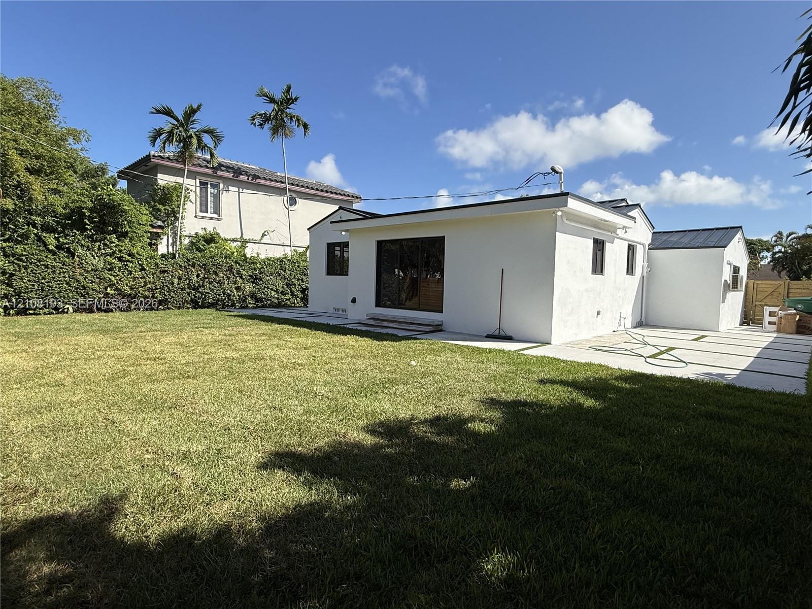 Backyard featuring a grass lawn, paved patio with inlay grass strips, sliding glass doors, and a perimeter hedge