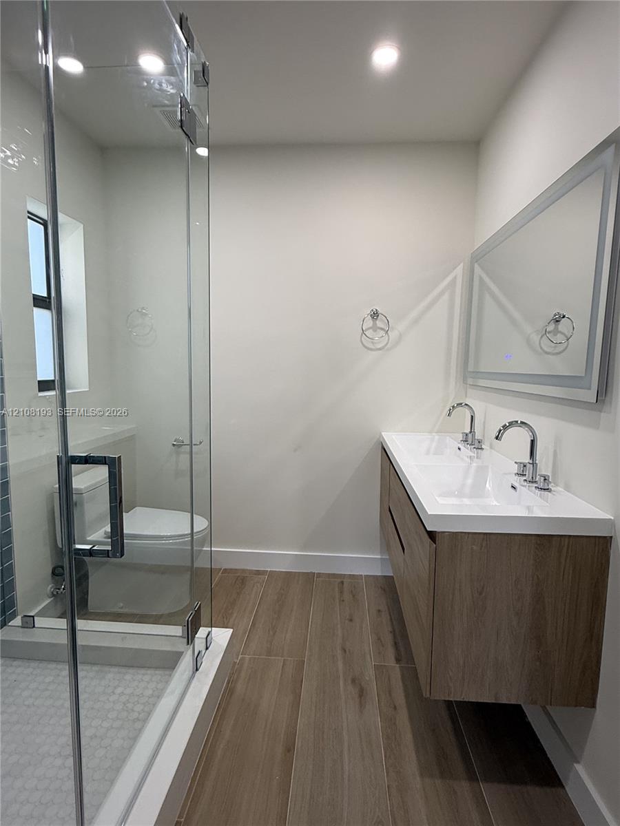 Floating vanity featuring a dual-sink integrated basin, wood-finish cabinetry, porcelain tile flooring, and a glass-enclosed shower with a modern chrome-finish hardware suite