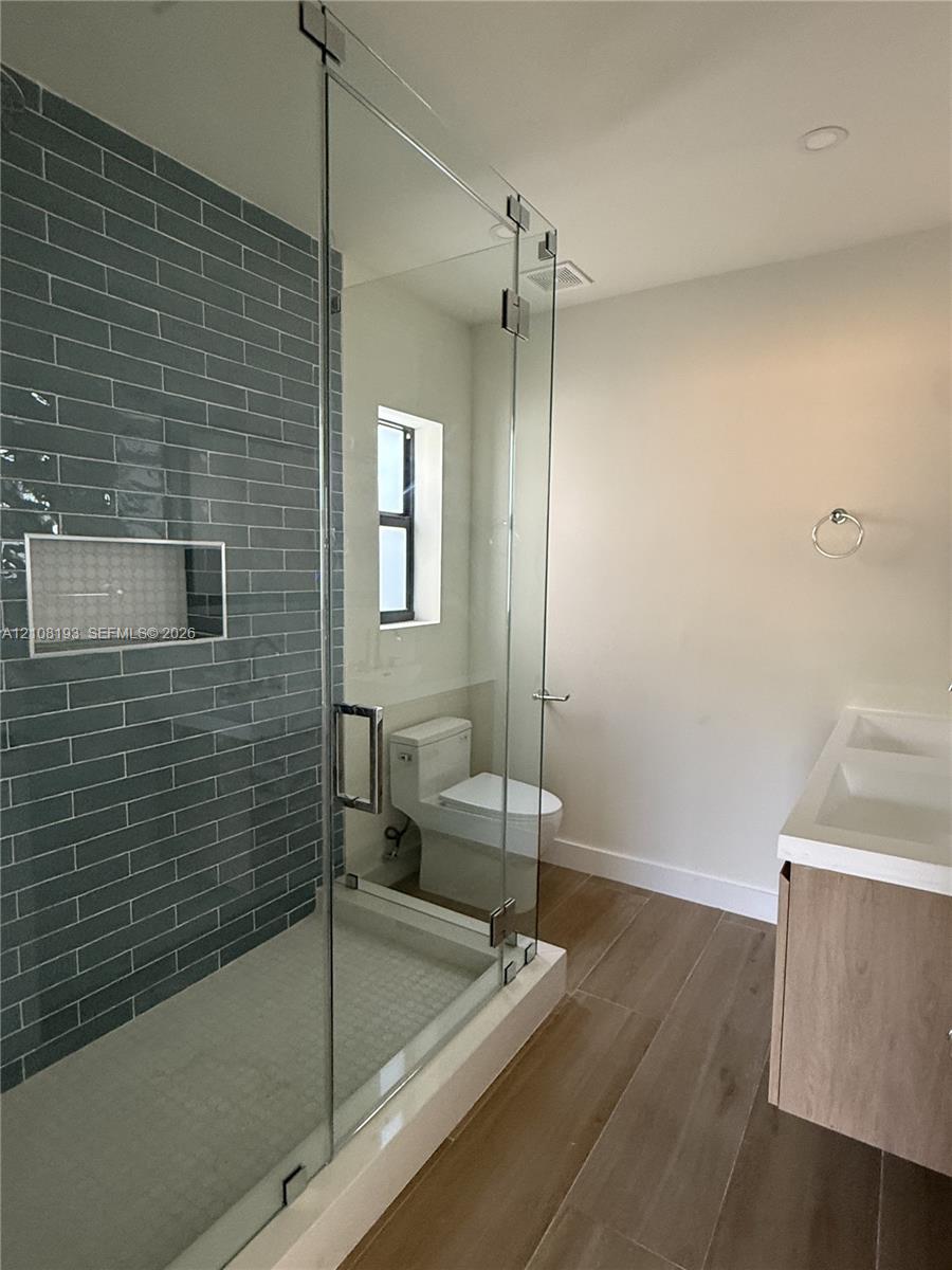 Walk-in shower featuring a glass enclosure, gray subway tile wall, and built-in recessed niche, complemented by wood-finish flooring and a floating dual-sink vanity