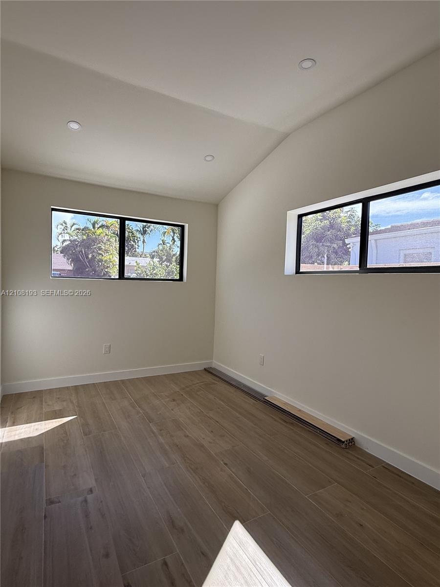 Room interior featuring wood-finish flooring, vaulted ceilings, recessed lighting, and horizontal windows with black framing