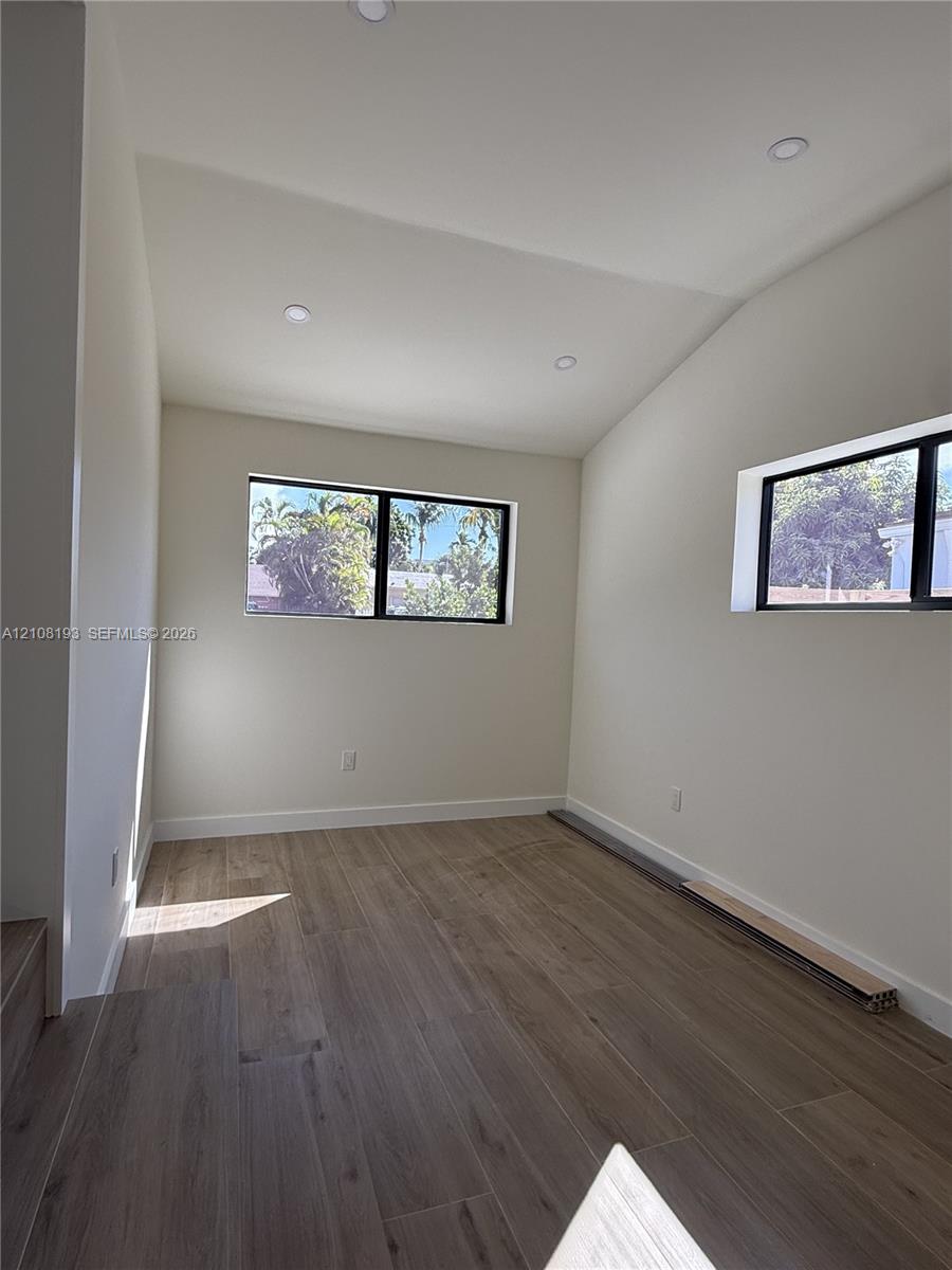 Vaulted ceiling with recessed lighting, wood-finish flooring, and black-framed windows