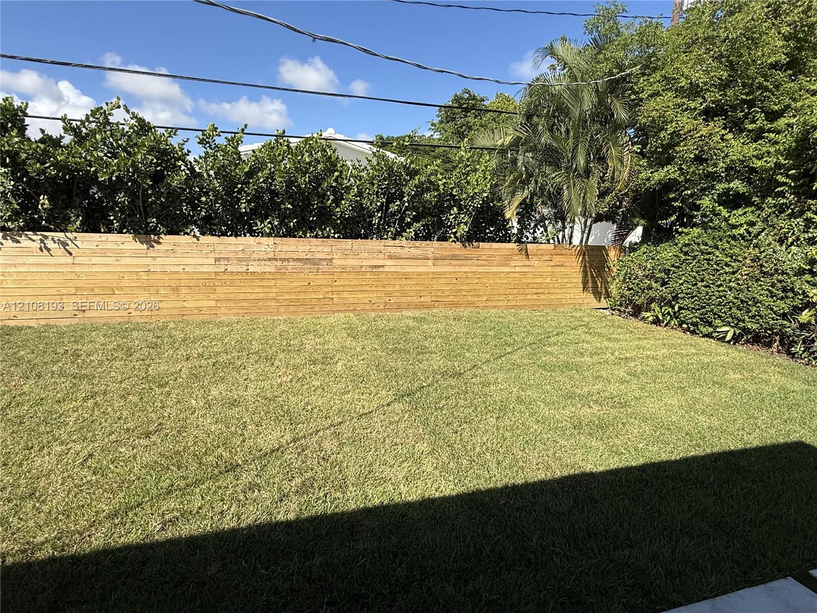 Backyard featuring a horizontal wood-slat privacy fence, manicured lawn, and mature perimeter landscaping