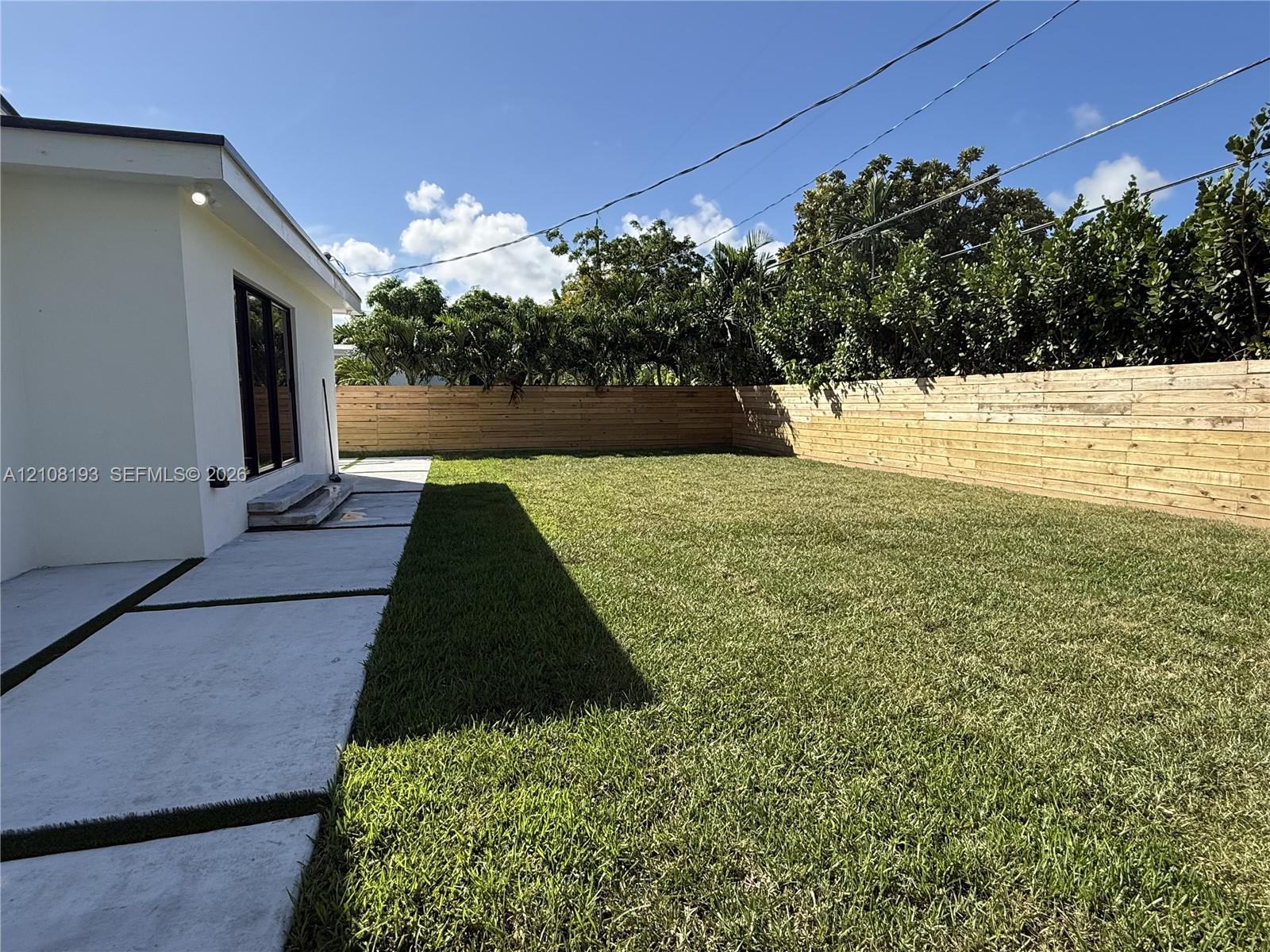 Rear exterior featuring a level grass lawn, horizontal wood perimeter fencing, and concrete paver patio with turf inlay