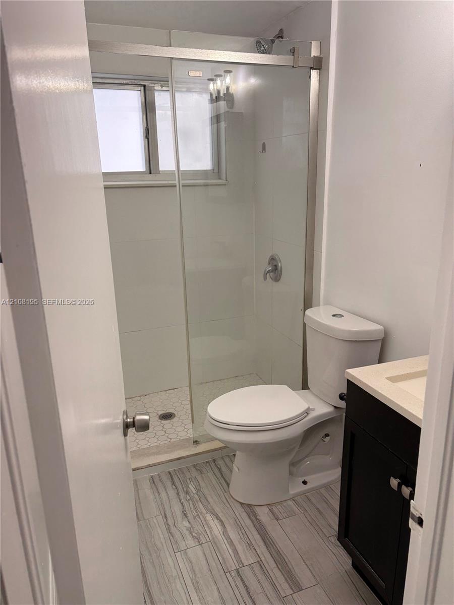 Walk-in shower with a sliding glass door, white tile surround, and hexagonal floor tiling, complemented by a single-sink vanity with dark-finish cabinetry and a light-toned countertop