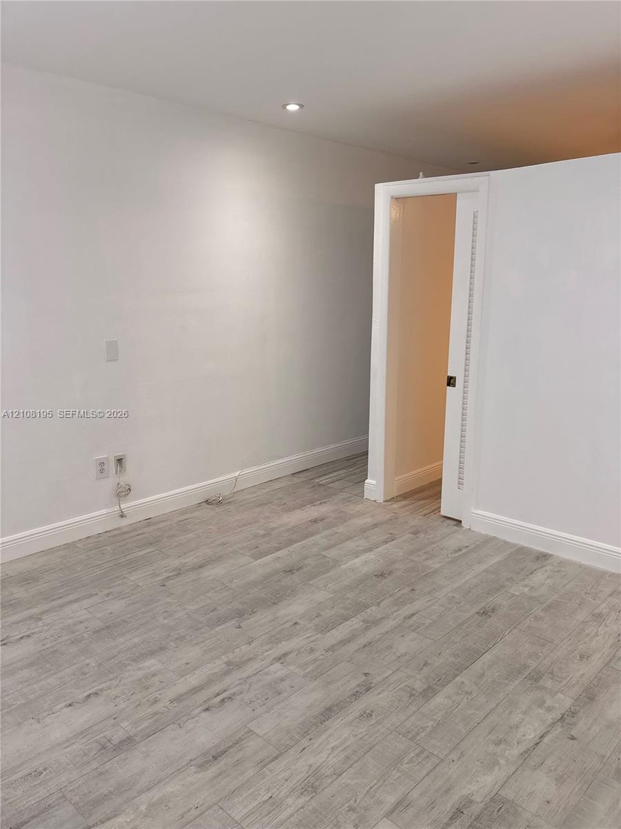 Interior space featuring wood-finish flooring, recessed ceiling lighting, and a white interior door with a louvered panel