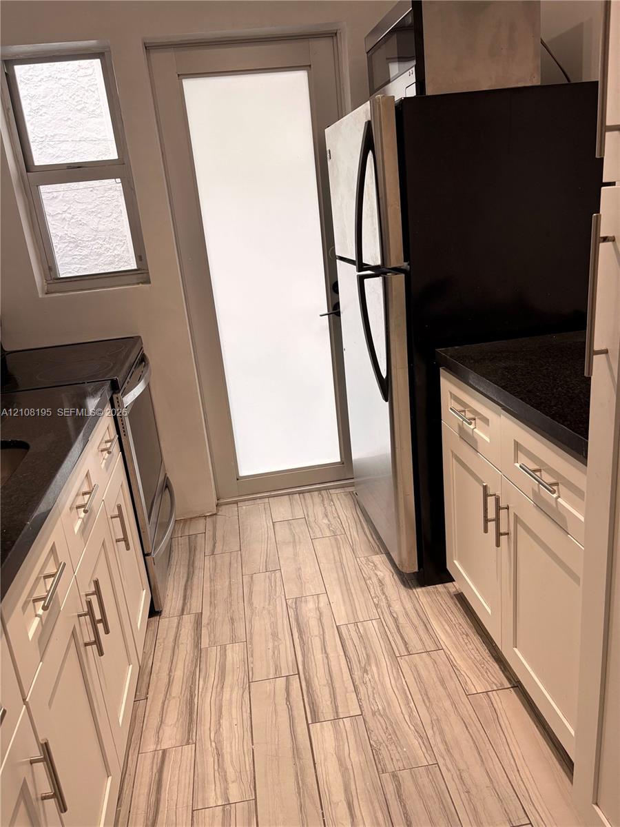 Kitchen featuring white shaker-style cabinetry, dark stone countertops, wood-finish tile flooring, a glass-panel exterior door, and stainless steel appliances