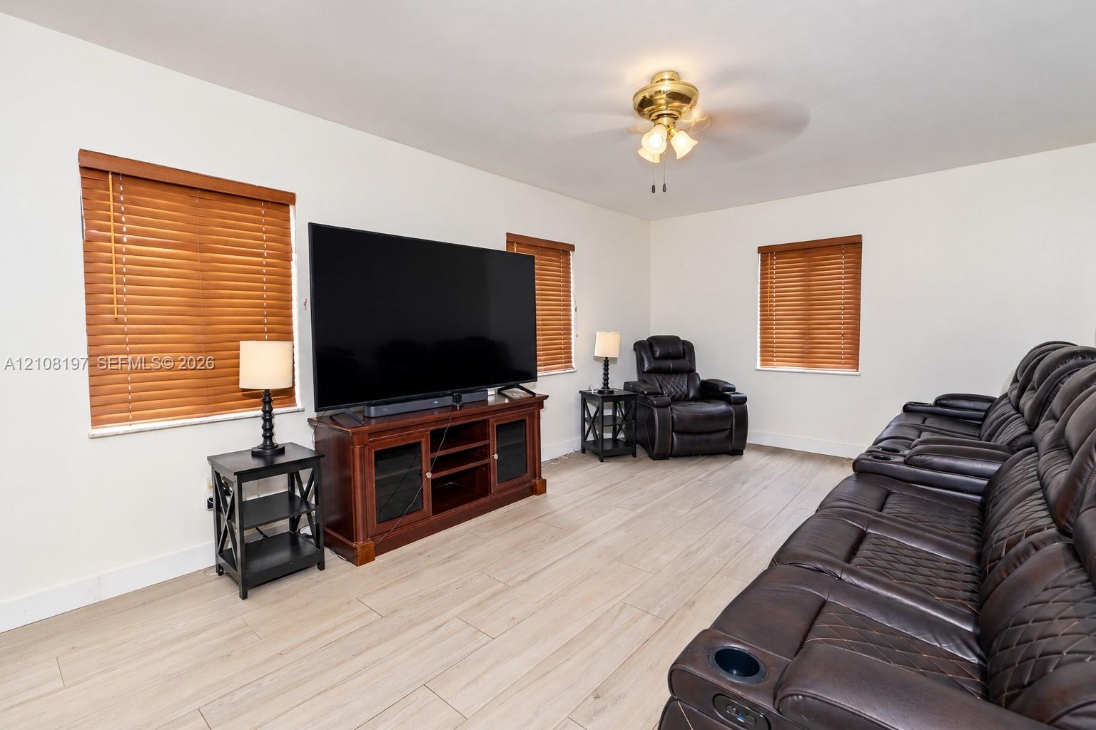 Wood-finish plank flooring, neutral wall tones, multi-pane window treatments, and a ceiling-mounted light fixture with integrated fan