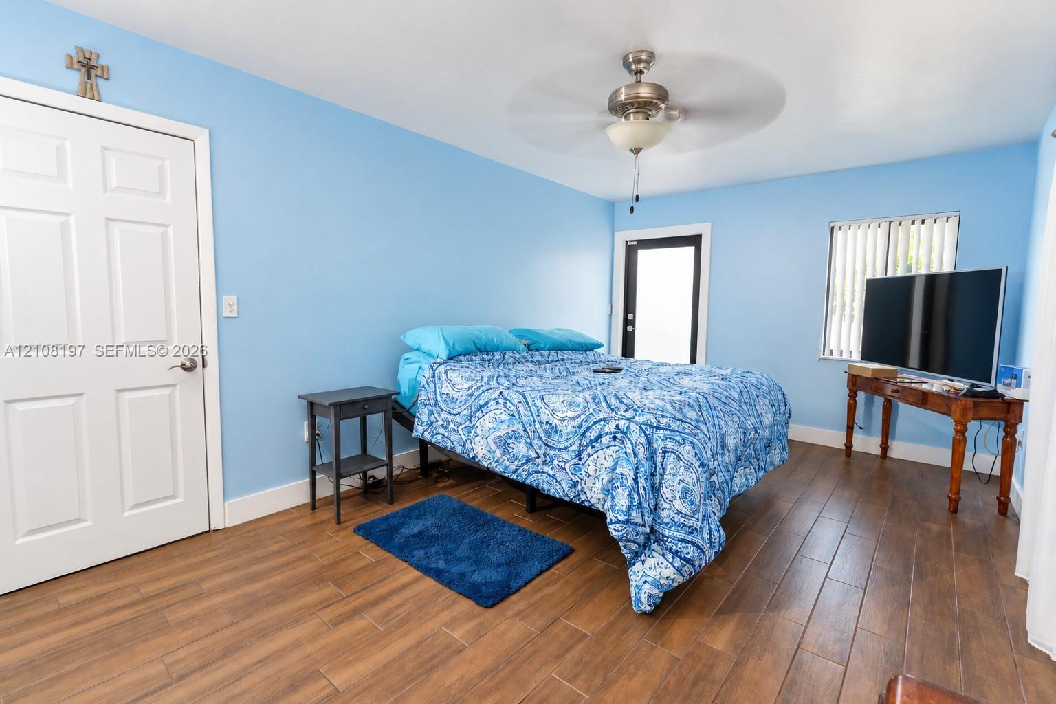 Room featuring wood-finish tile flooring, ceiling fan with light fixture, multi-paneled door, and exterior access door