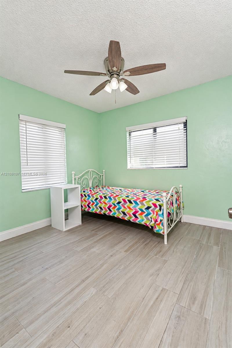 Room featuring wood-finish tile flooring, two windows with horizontal blinds, and a ceiling fan with integrated light fixture
