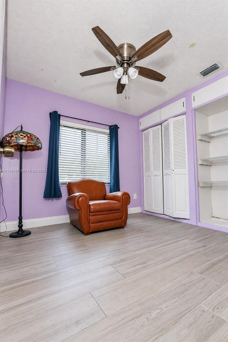 Wood-finish flooring, ceiling fan with integrated lighting, dual bifold closet doors, and open shelving