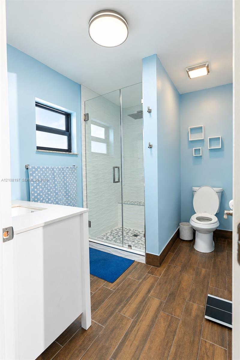 Bathroom featuring wood-finish flooring, a white vanity, a walk-in glass-enclosed shower with a built-in bench, and textured wall tile