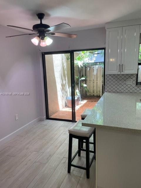 Kitchen featuring white shaker-style cabinetry, a quartz countertop, diamond-patterned tile backsplash, wood-finish flooring, and a sliding glass door