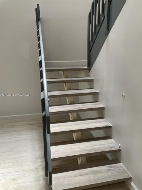 Open-riser staircase featuring wood-finish treads, a structural central support, and contrasting dark-toned railings