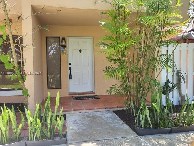 Covered entryway with terracotta tile flooring, four-panel entry door, integrated vertical side light, and exterior wall-mounted light fixture