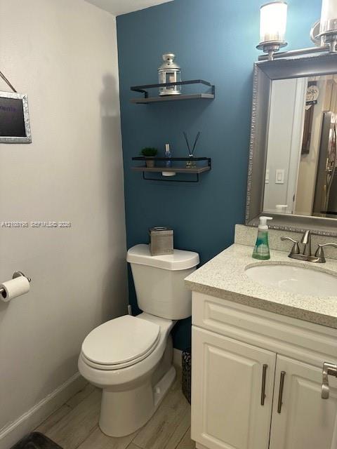 Vanity with light-toned solid surface countertop and undermount sink, white cabinetry with metallic pulls, wood-finish flooring, and wall-mounted shelving