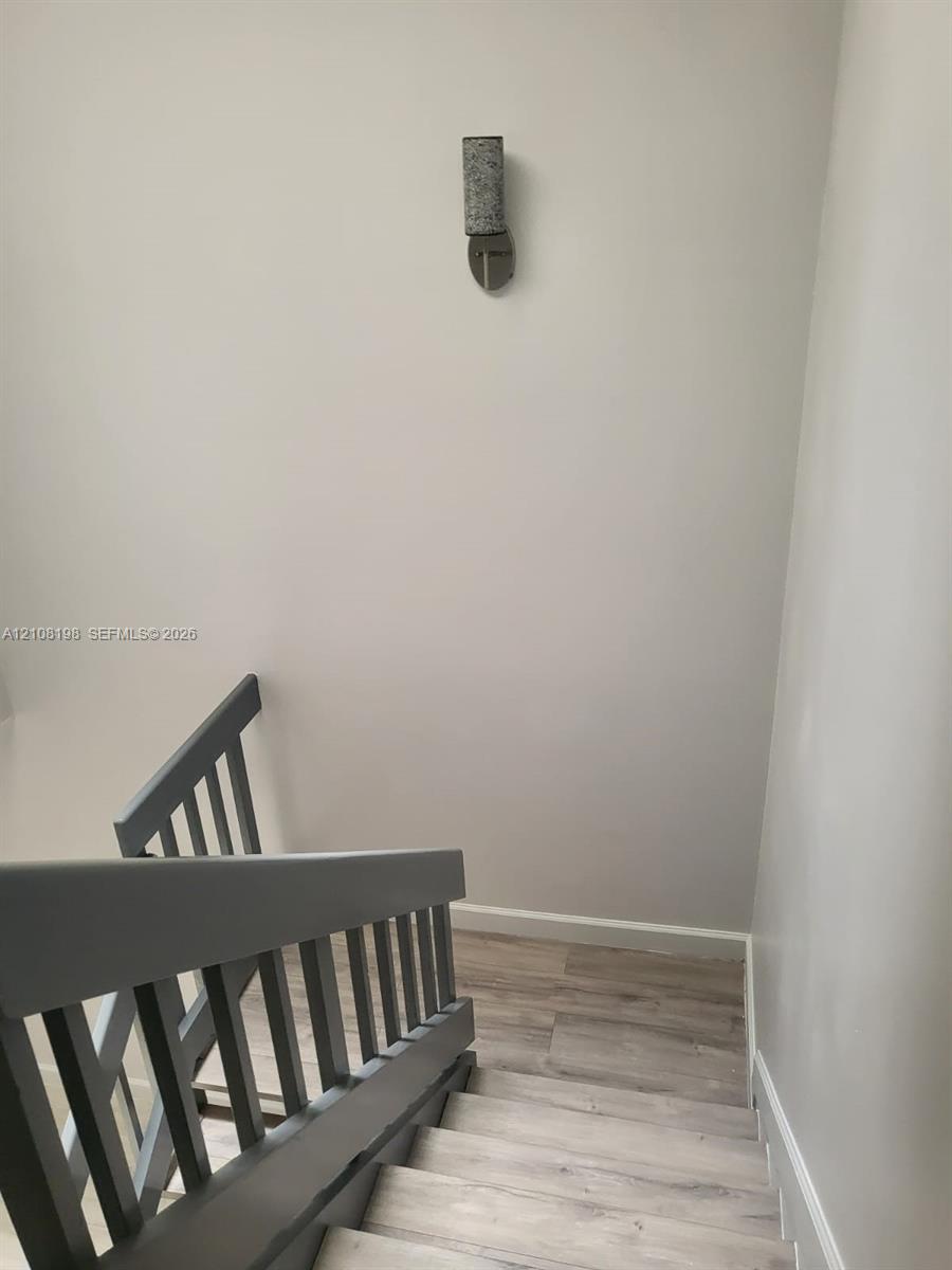 Staircase featuring wood-finish flooring, a painted wooden balustrade, and a cylindrical wall-mounted light fixture