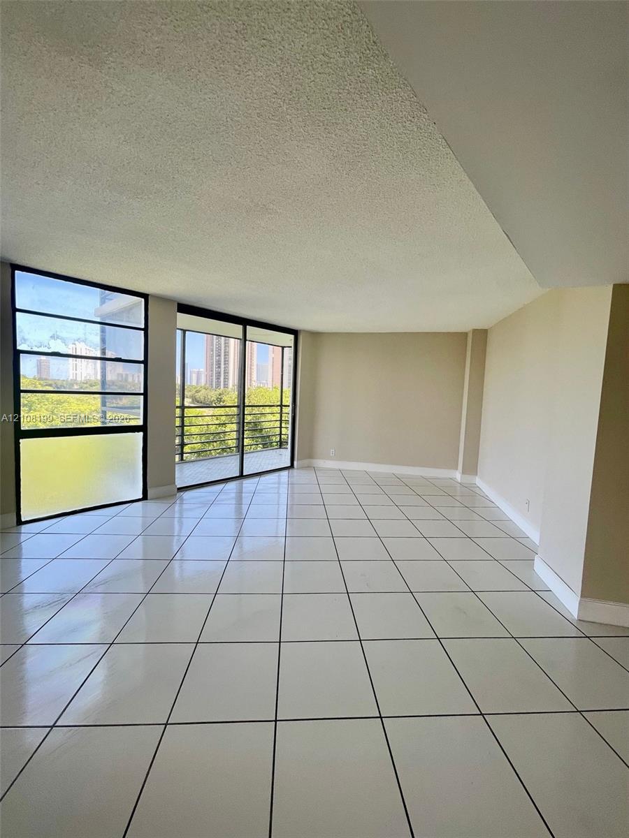Interior space featuring large-format tile flooring, expansive floor-to-ceiling windows, sliding glass door access to a balcony, and textured ceiling finish