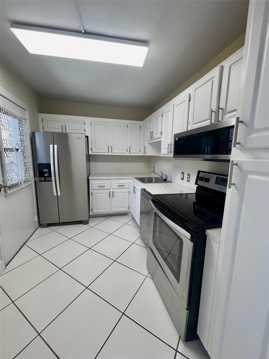 Kitchen featuring white cabinetry, stainless steel appliances, solid-surface countertops, and diagonal-set tile flooring Kitchen featuring white cabinetry, stainless steel appliances, solid-surface countertops, and diagonal-set tile flooring
