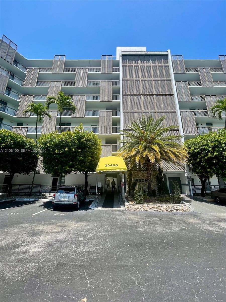 Multi-story residential building exterior featuring vertical louvered balcony privacy screens, stone veneer facade accents, a covered entryway, and established palm tree landscaping