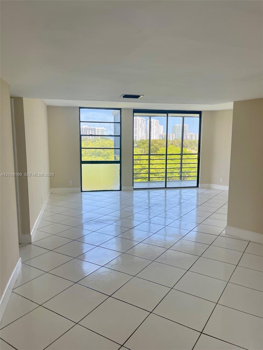 Open-concept interior featuring large-format diagonal tile flooring, floor-to-ceiling windows, and sliding glass doors leading to a screened balcony Open-concept interior featuring large-format diagonal tile flooring, floor-to-ceiling windows, and sliding glass doors leading to a screened balcony