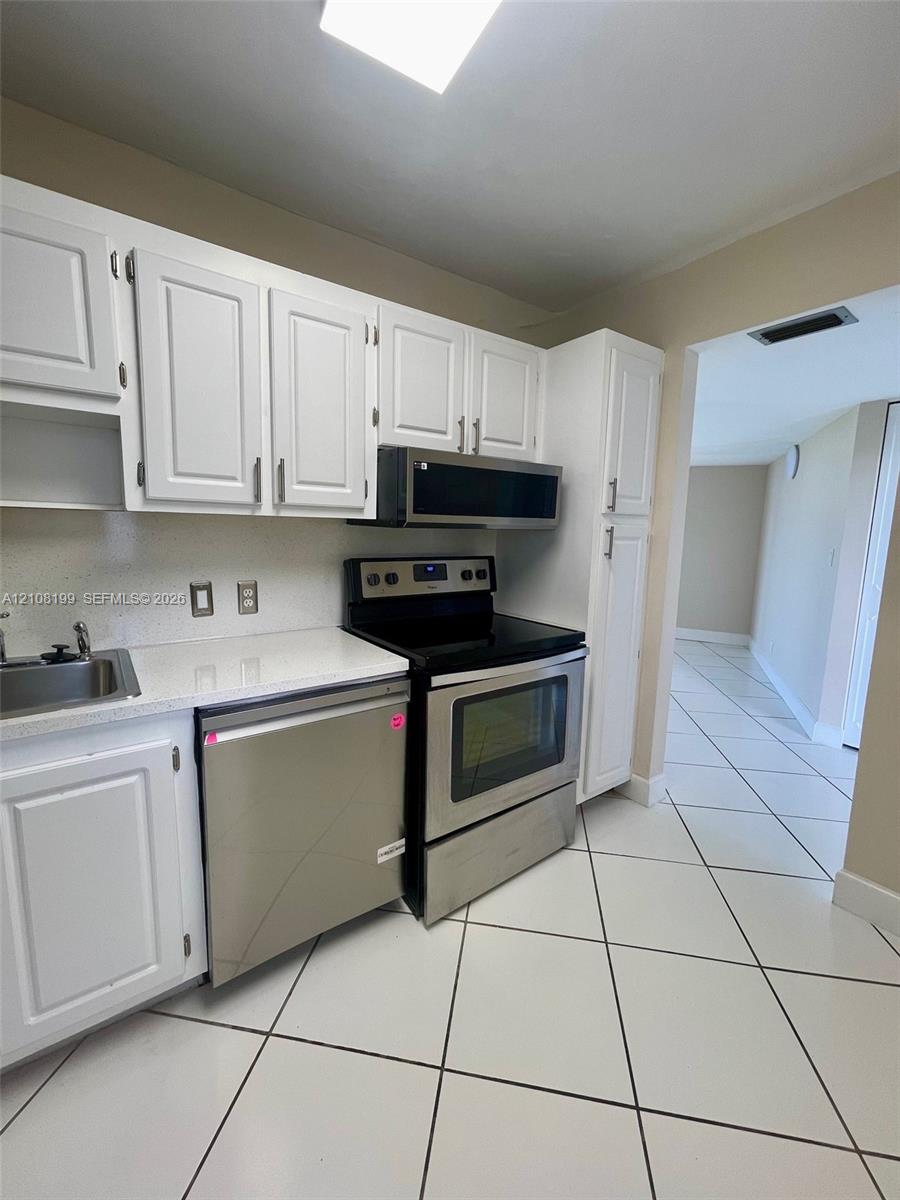 Kitchen featuring white cabinetry, stone-finish countertops, stainless steel appliances, and tile flooring Kitchen featuring white cabinetry, stone-finish countertops, stainless steel appliances, and tile flooring