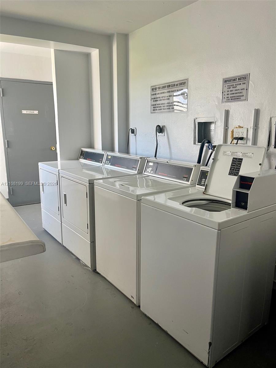 Laundry facility featuring multiple top-load washers and front-load dryers, solid-surface flooring, and a grey flush-panel door Laundry facility featuring multiple top-load washers and front-load dryers, solid-surface flooring, and a grey flush-panel door