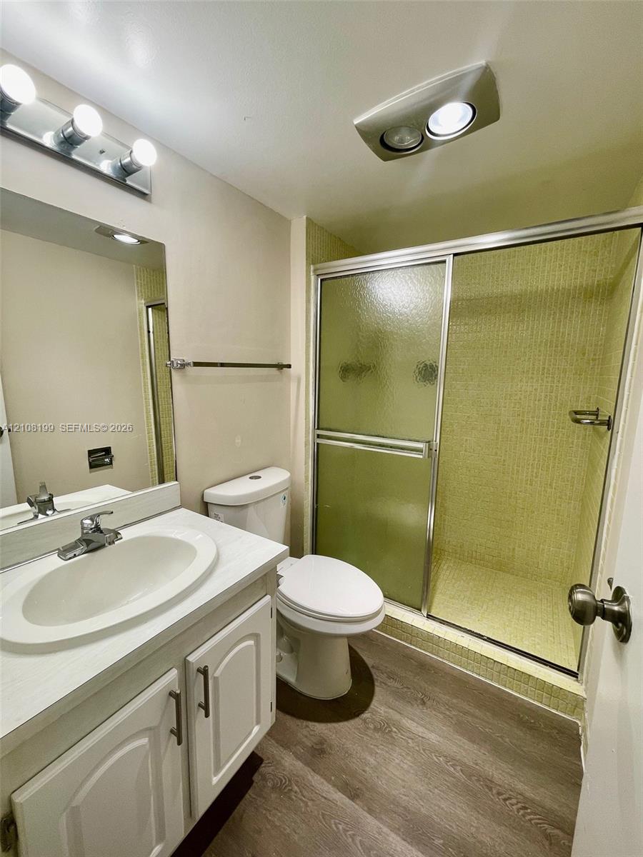 Bathroom featuring a white vanity with an integrated oval sink, wood-finish flooring, and a walk-in shower with a sliding glass door and tiled surround
