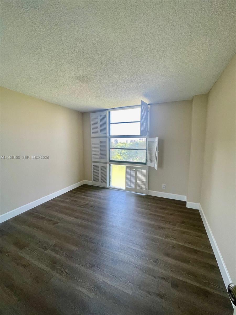 Room featuring wood-finish flooring, multi-pane window with louvered shutters, and textured ceiling