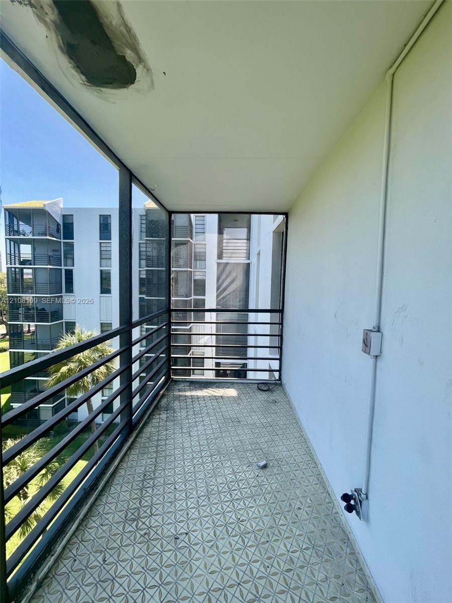Covered balcony featuring patterned tile flooring, dark metal railing, and exposed electrical fixture