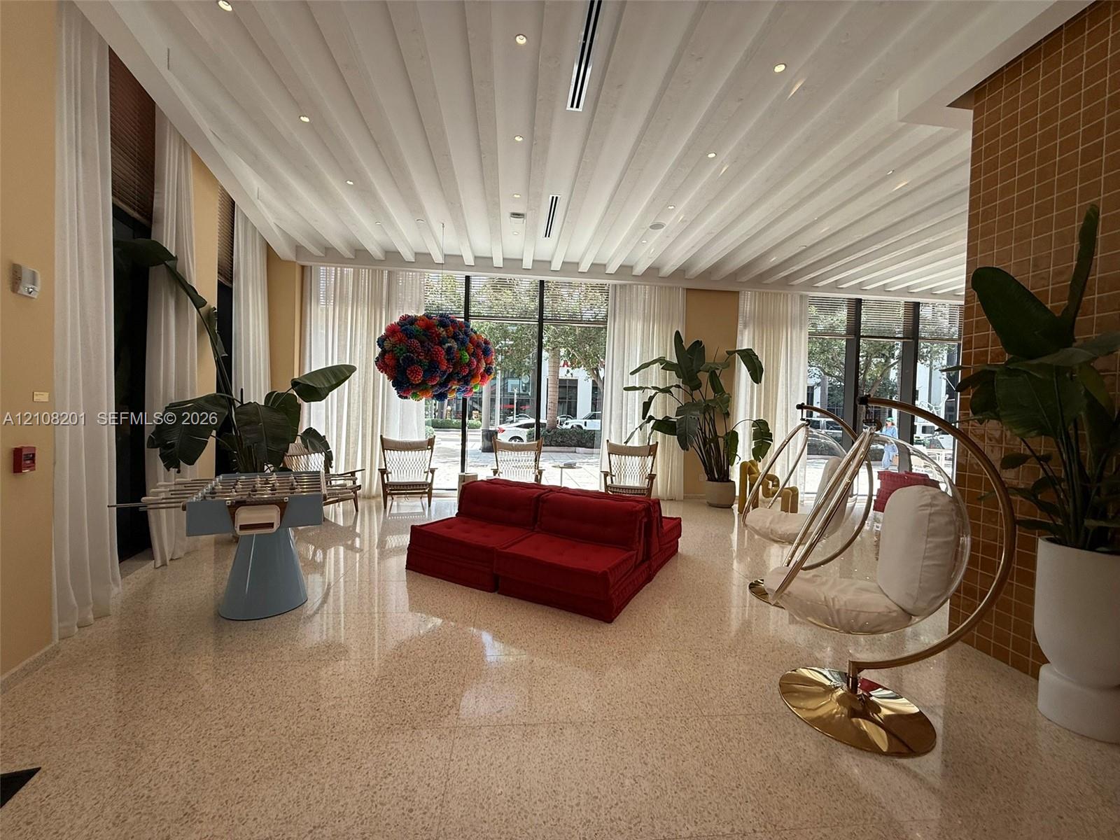 Common area featuring high, vaulted ceilings with recessed lighting, full-height floor-to-ceiling windows, polished stone-finish flooring, and a decorative grid-patterned accent wall
