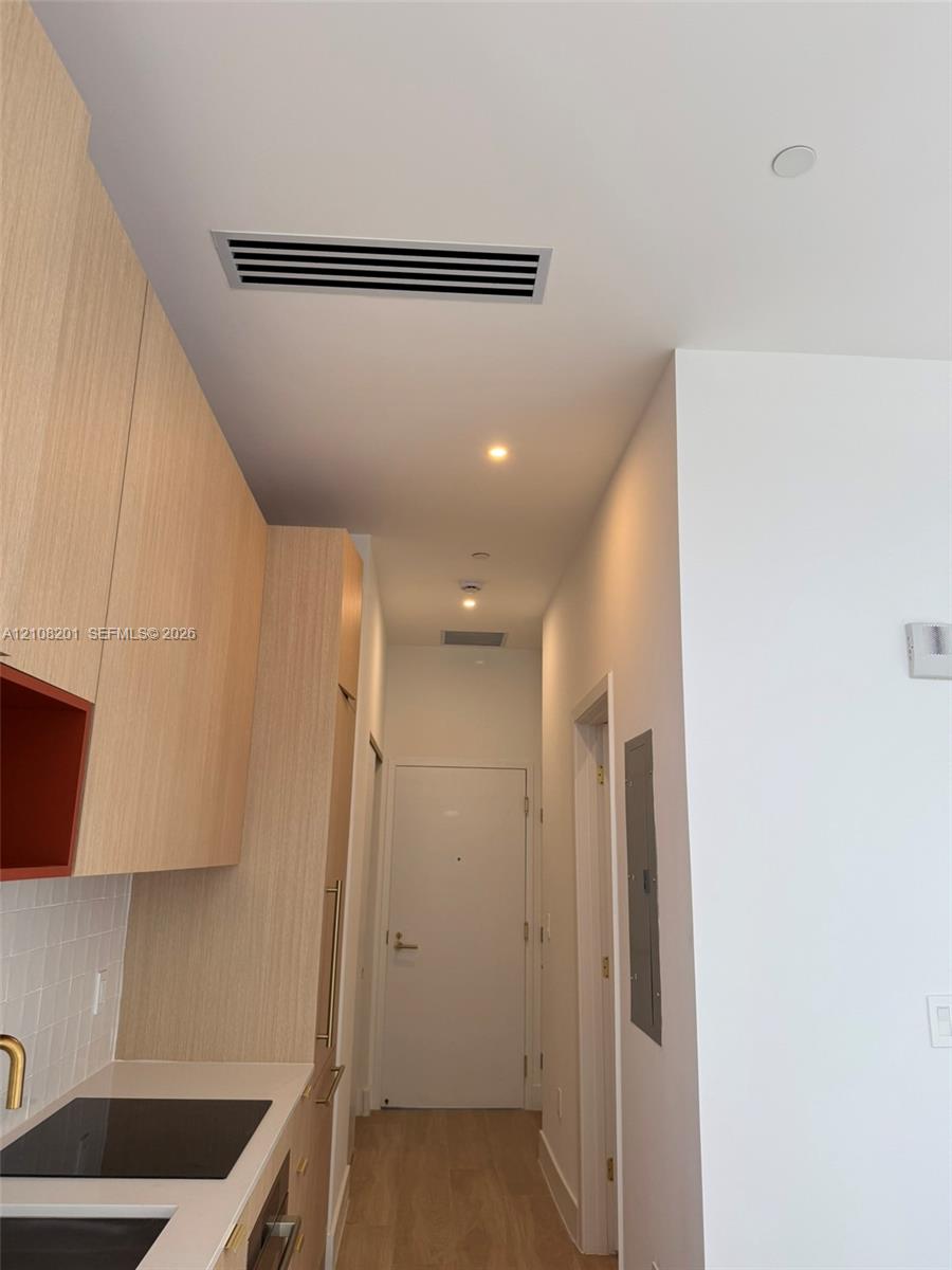 Light wood-finish cabinetry, white tile backsplash, solid surface countertop, recessed ceiling lighting, and light-toned wood-finish flooring Light wood-finish cabinetry, white tile backsplash, solid surface countertop, recessed ceiling lighting, and light-toned wood-finish flooring