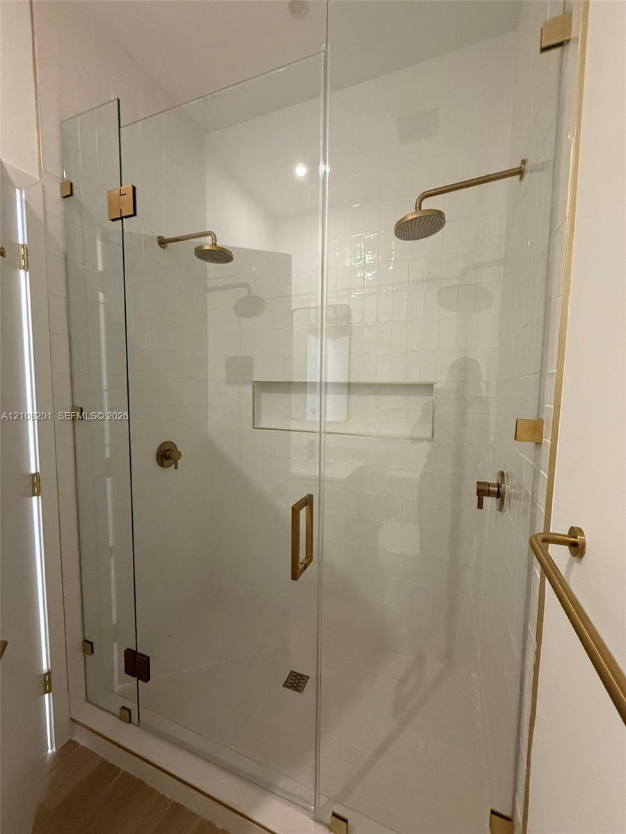 Walk-in shower featuring a frameless glass enclosure, dual wall-mounted shower heads, built-in recessed storage niche, and gold-finish hardware Walk-in shower featuring a frameless glass enclosure, dual wall-mounted shower heads, built-in recessed storage niche, and gold-finish hardware