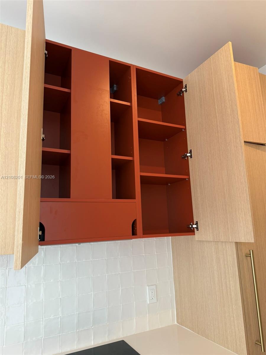 Custom cabinetry featuring wood-finish doors, interior shelving with a matte-finish rust-tone backing, and square-profile white tile backsplash Custom cabinetry featuring wood-finish doors, interior shelving with a matte-finish rust-tone backing, and square-profile white tile backsplash