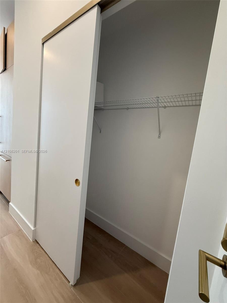 Sliding door closet featuring a brass-tone hardware track, recessed circular brass pull, wood-finish flooring, and integrated wire shelving Sliding door closet featuring a brass-tone hardware track, recessed circular brass pull, wood-finish flooring, and integrated wire shelving