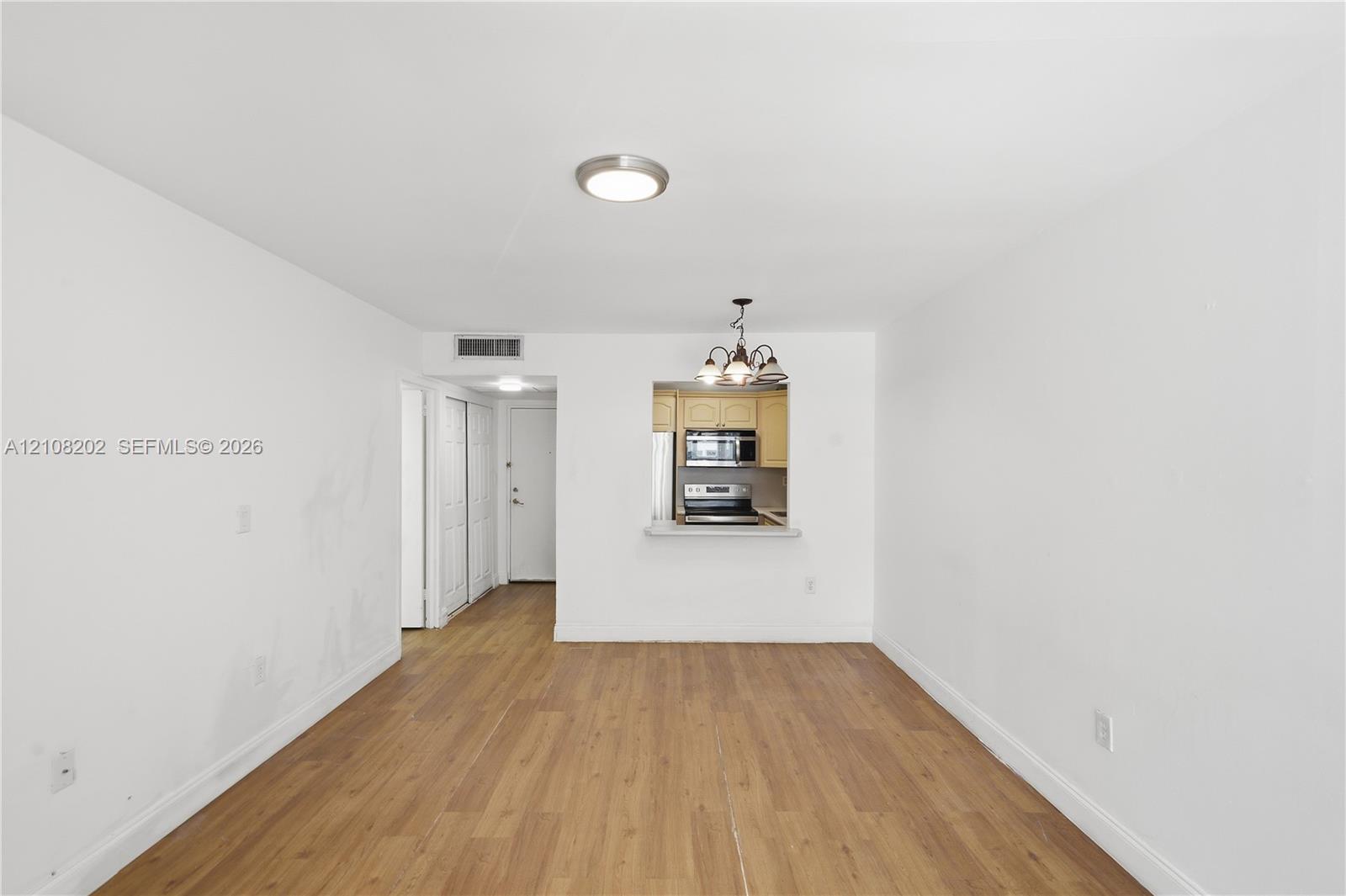 Interior space featuring wood-finish flooring, recessed ceiling lighting, a pass-through opening to the kitchen, and a kitchen featuring stainless steel appliances Interior space featuring wood-finish flooring, recessed ceiling lighting, a pass-through opening to the kitchen, and a kitchen featuring stainless steel appliances