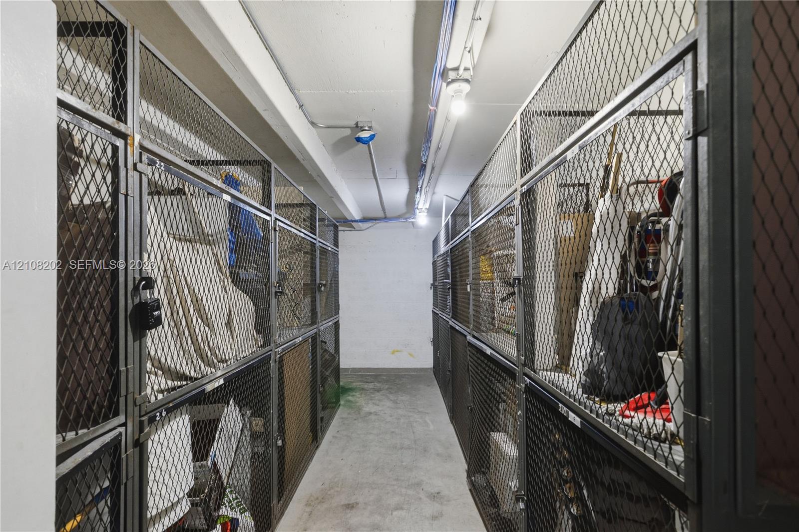 Dedicated storage area featuring secure, floor-to-ceiling metal wire mesh lockers, concrete flooring, and exposed ceiling lighting