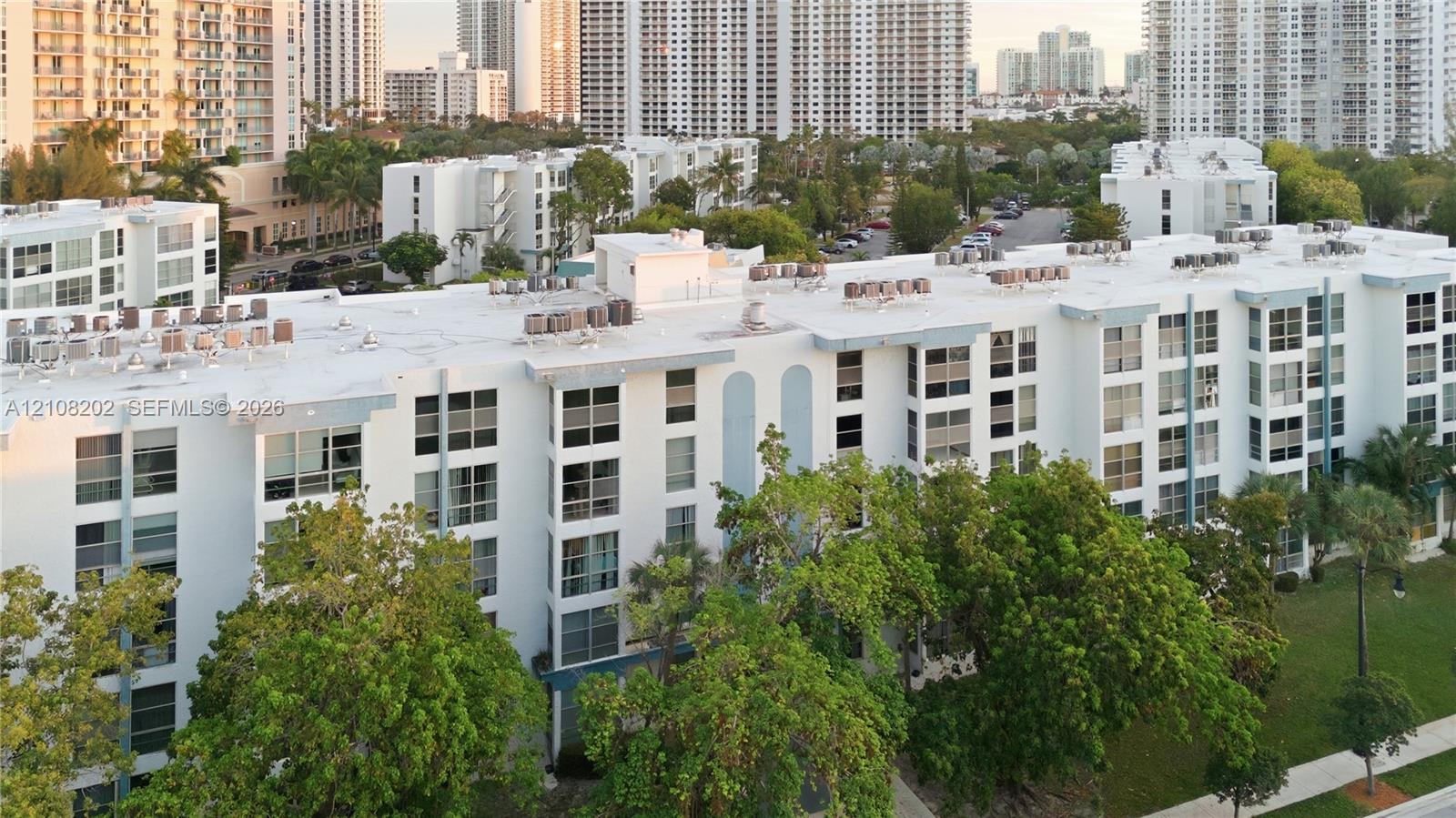 Mid-rise residential building featuring a white facade, multi-level structural design, uniform window grid, and integrated green space with mature trees