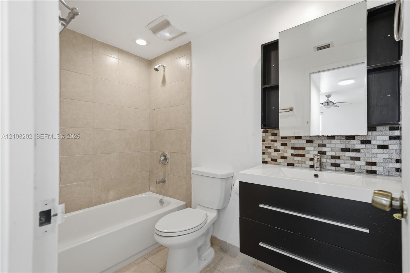 Bathroom featuring a floating dark-finish vanity with an integrated basin, multi-toned mosaic tile backsplash, medicine cabinet, and a bathtub with beige wall tiling Bathroom featuring a floating dark-finish vanity with an integrated basin, multi-toned mosaic tile backsplash, medicine cabinet, and a bathtub with beige wall tiling