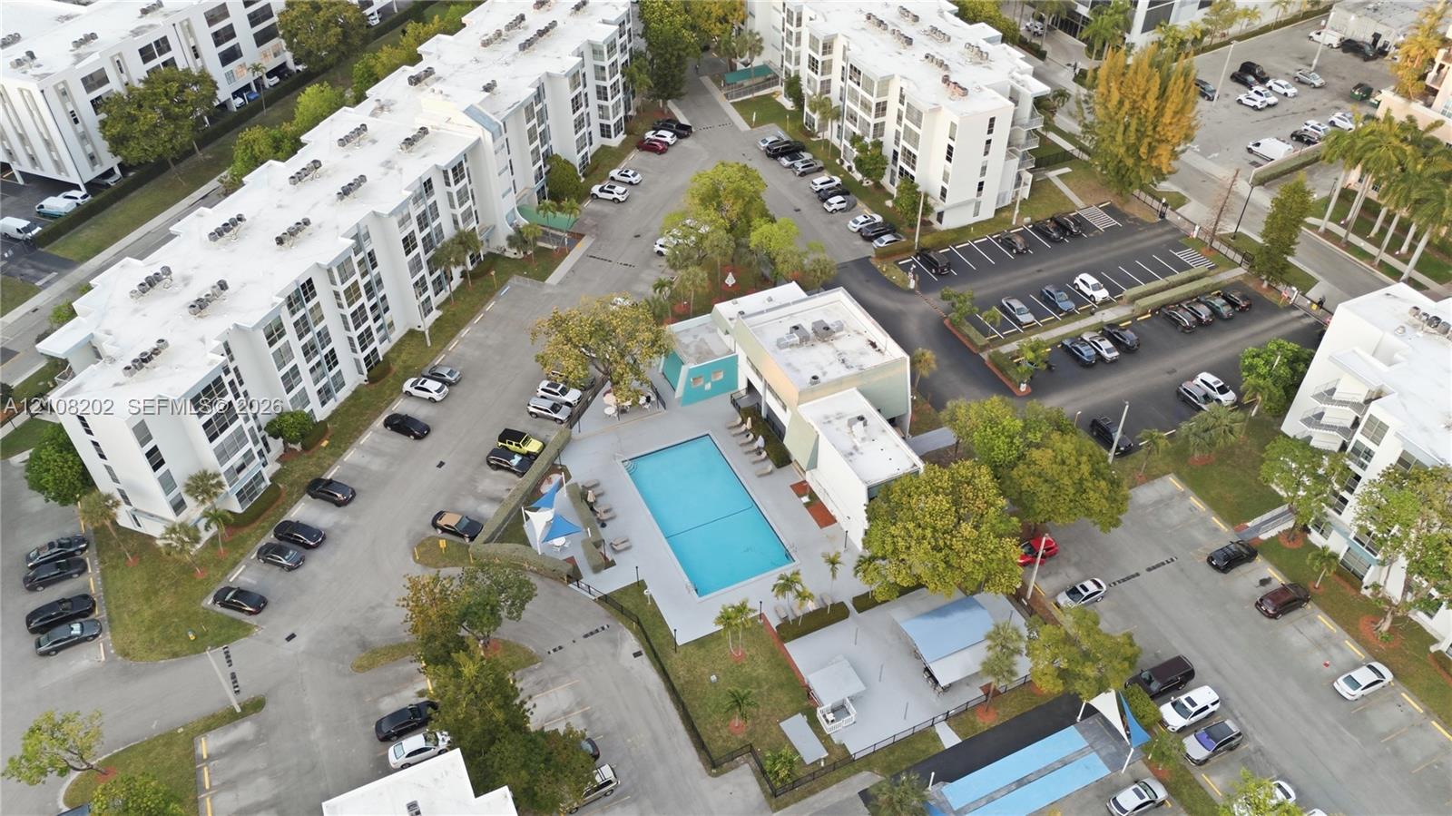 Aerial perspective featuring a communal swimming pool, paved surface parking areas, and mature landscaping