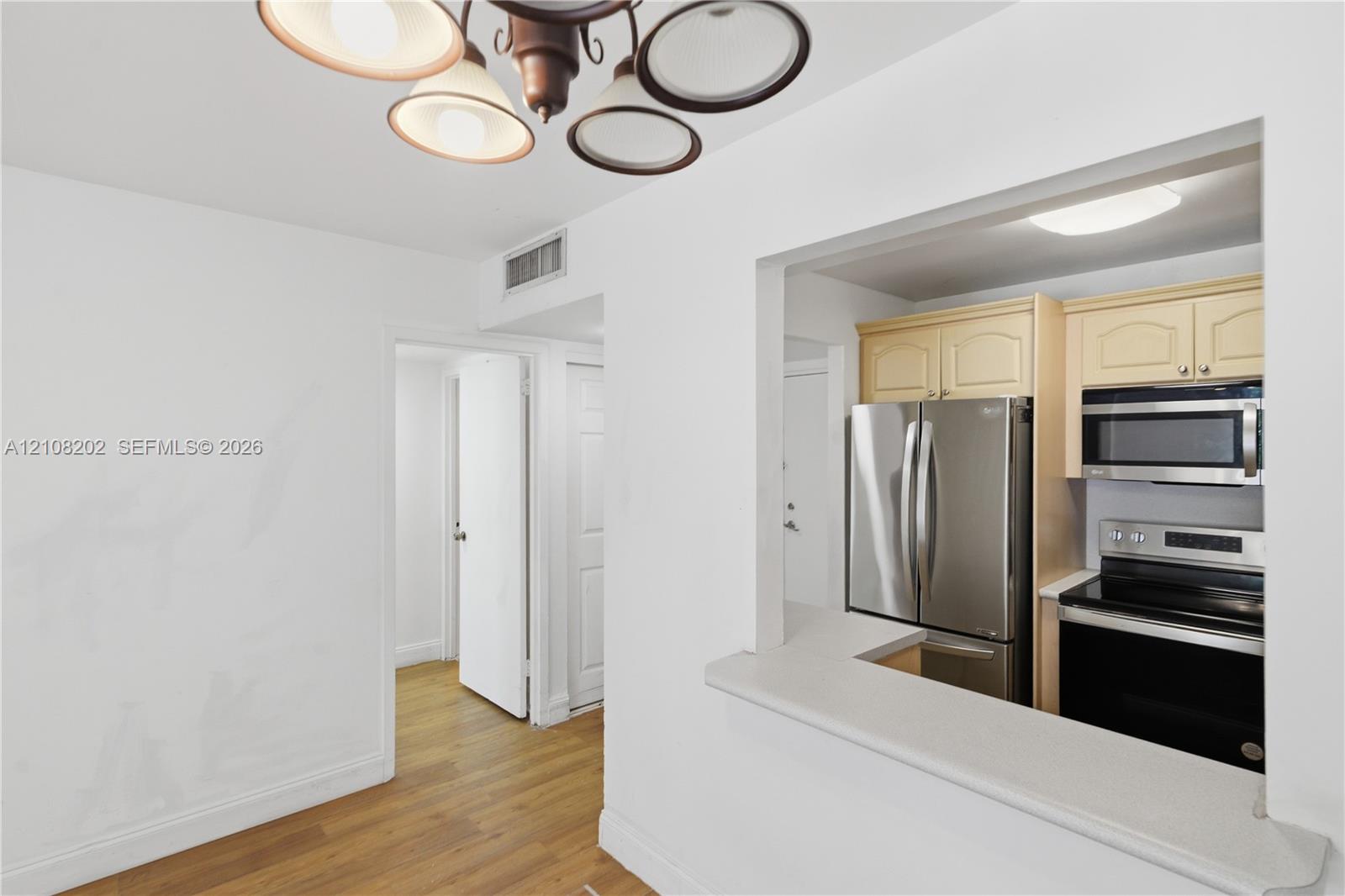 Kitchen featuring a pass-through opening, stone-finish countertops, stainless steel appliances, wood-finish flooring, and a multi-light chandelier Kitchen featuring a pass-through opening, stone-finish countertops, stainless steel appliances, wood-finish flooring, and a multi-light chandelier